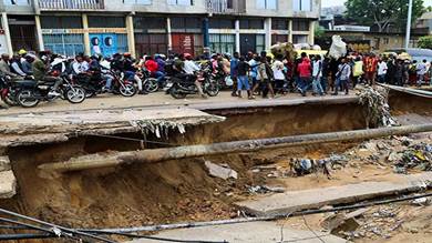 مواطنون يعبرون طريقاً رئيسياً انهار تماماً بعد أن تسببت الأمطار الغزيرة في حدوث فيضانات وانهيارات أرضية في ضواحي كينشاسا الكونغو الديمقراطية